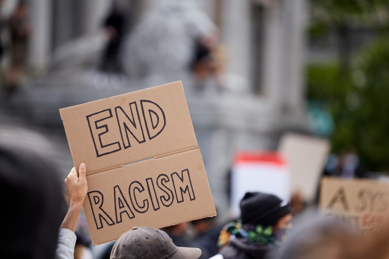 Protestors holding signs in the street, the one in focus displays 'End Racism'