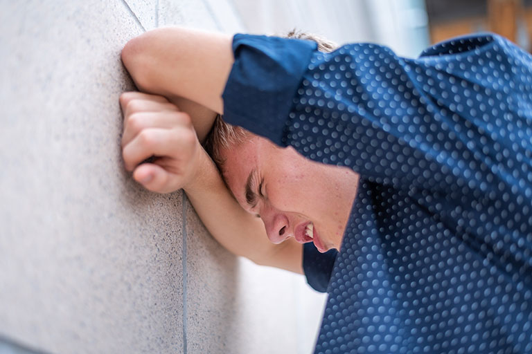 An upset teen resting their head against a wall trying to calm down